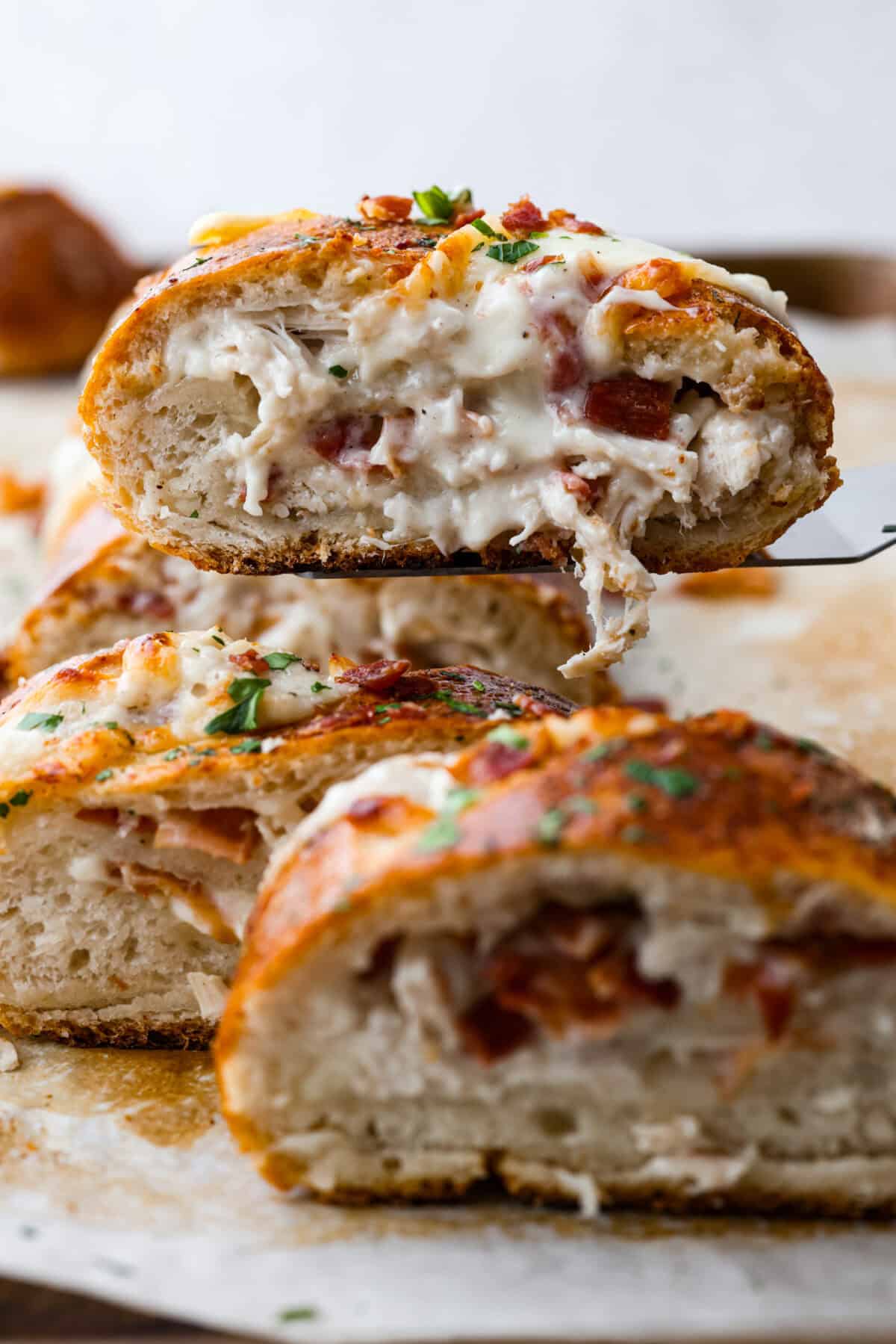 Side shot of someone lifting a piece of the chicken bacon wrapped Stromboli with a spatula. 