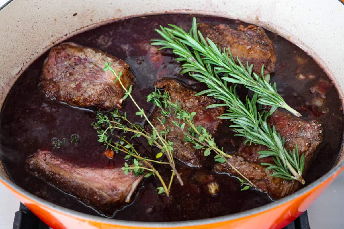 Sixth photo of the short ribs added back to the pot with fresh herbs.