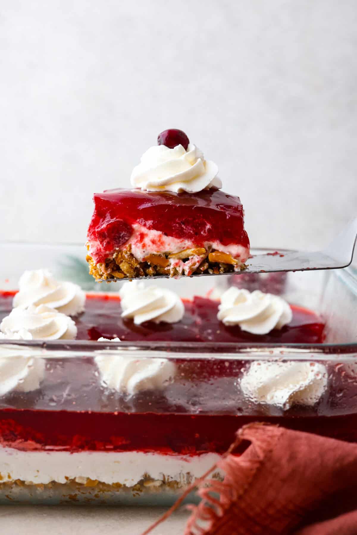 Close side view of a spatula lifting a slice of cranberry pretzel salad from the baking dish.