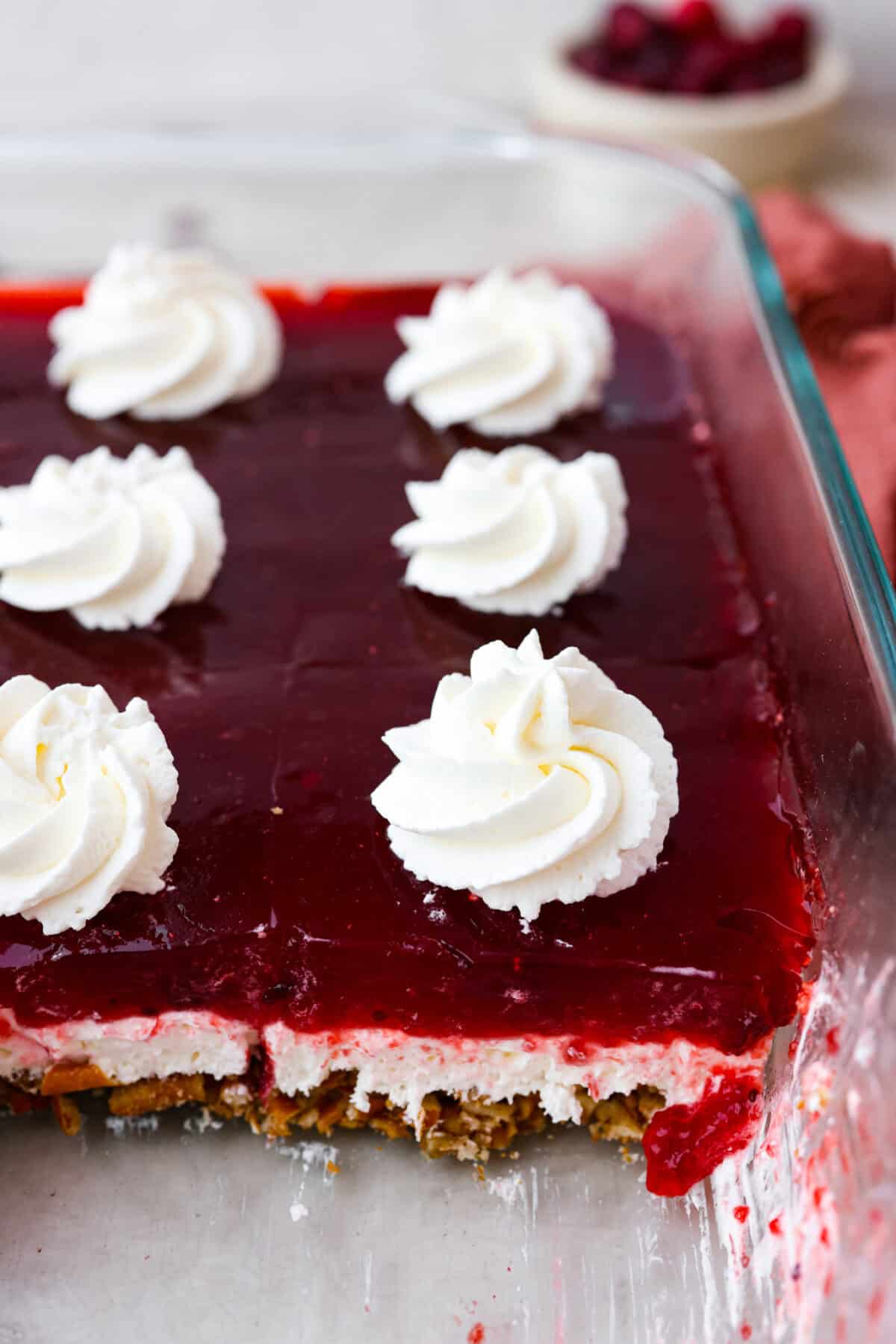 Close top view of cranberry pretzel salad in a baking dish with dollops of whipped cream on top.