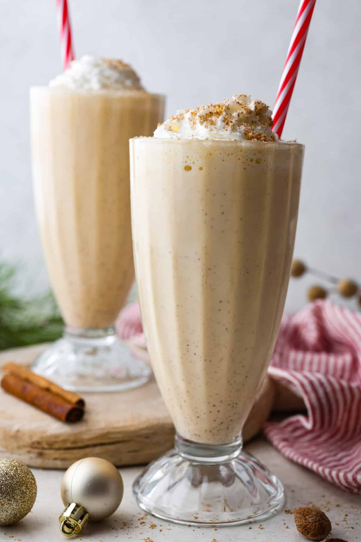 Side shot of two glasses full of eggnog milkshake with festive straw. 