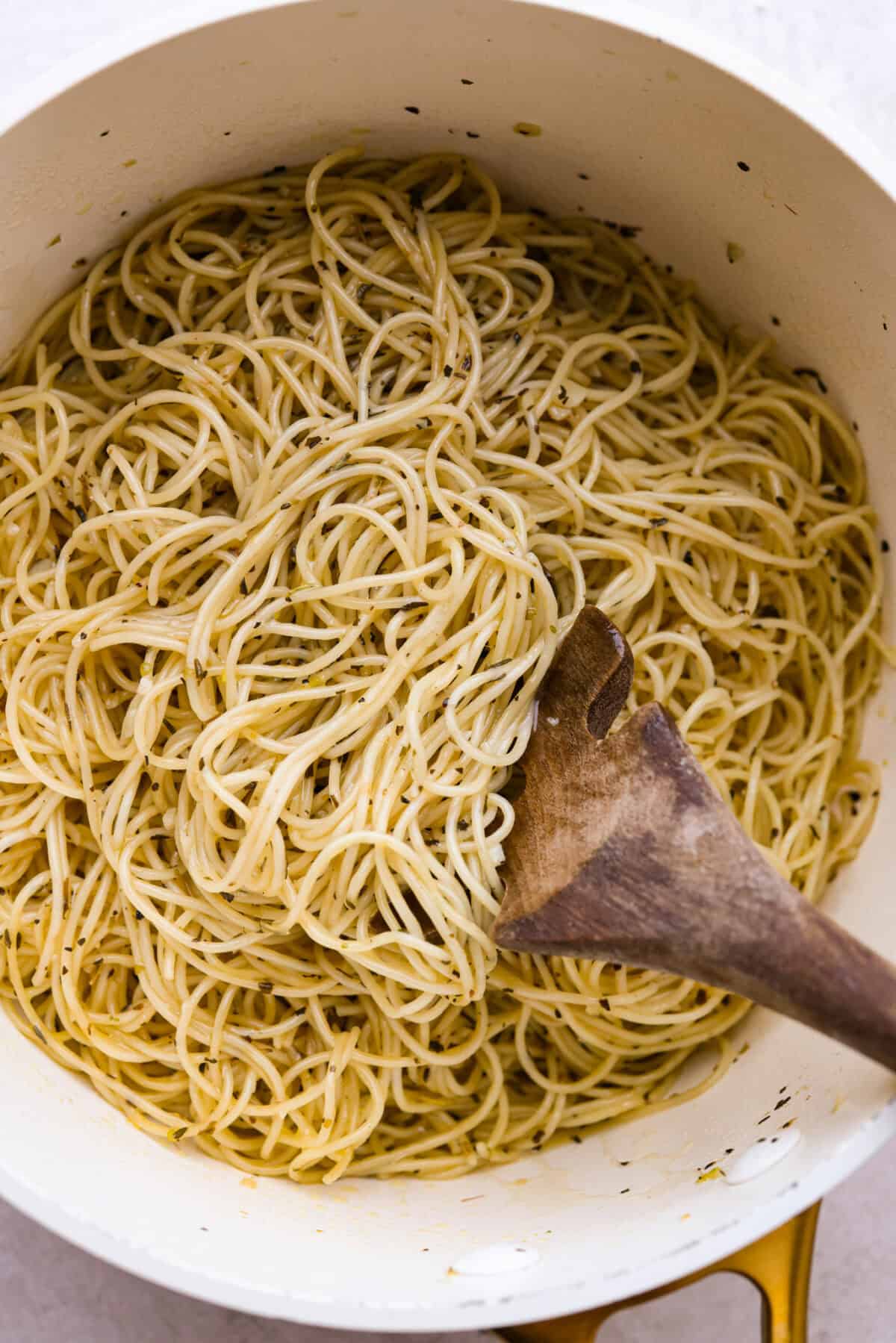 Overhead shot of garlic butter pasta in a pot with wooden slotted spoon. 