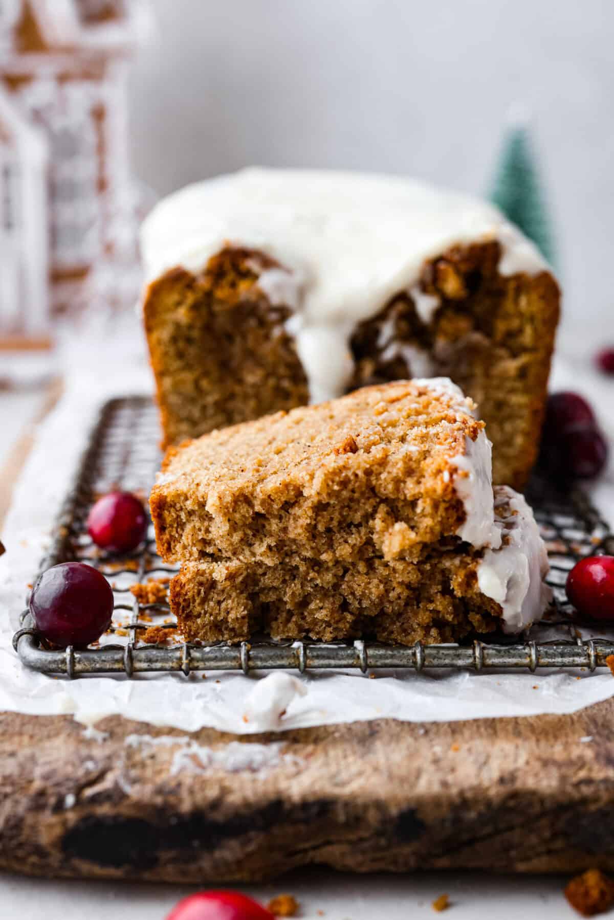 Side shot of gingerbread loaf slice torn in half on a cooling rack in front of the whole loaf. 