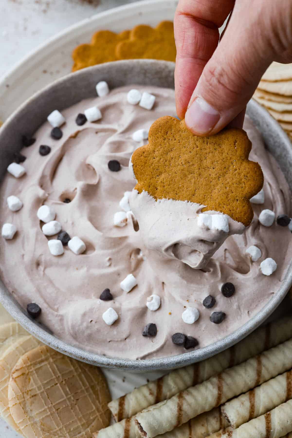 Close up shot of someone dipping a cookie into the hot cocoa dip. 