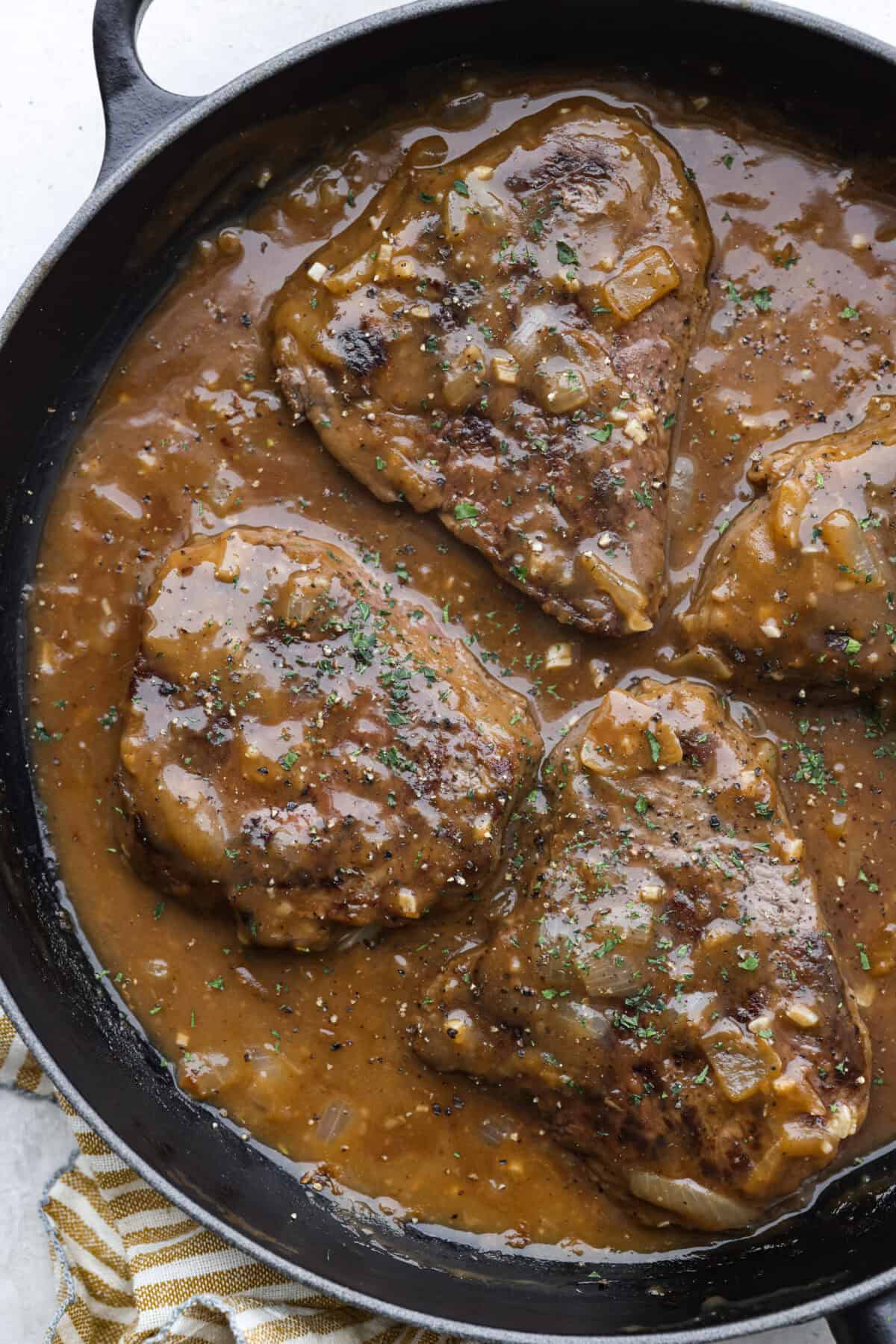 Overhead shot of smothered steak in a skillet. 