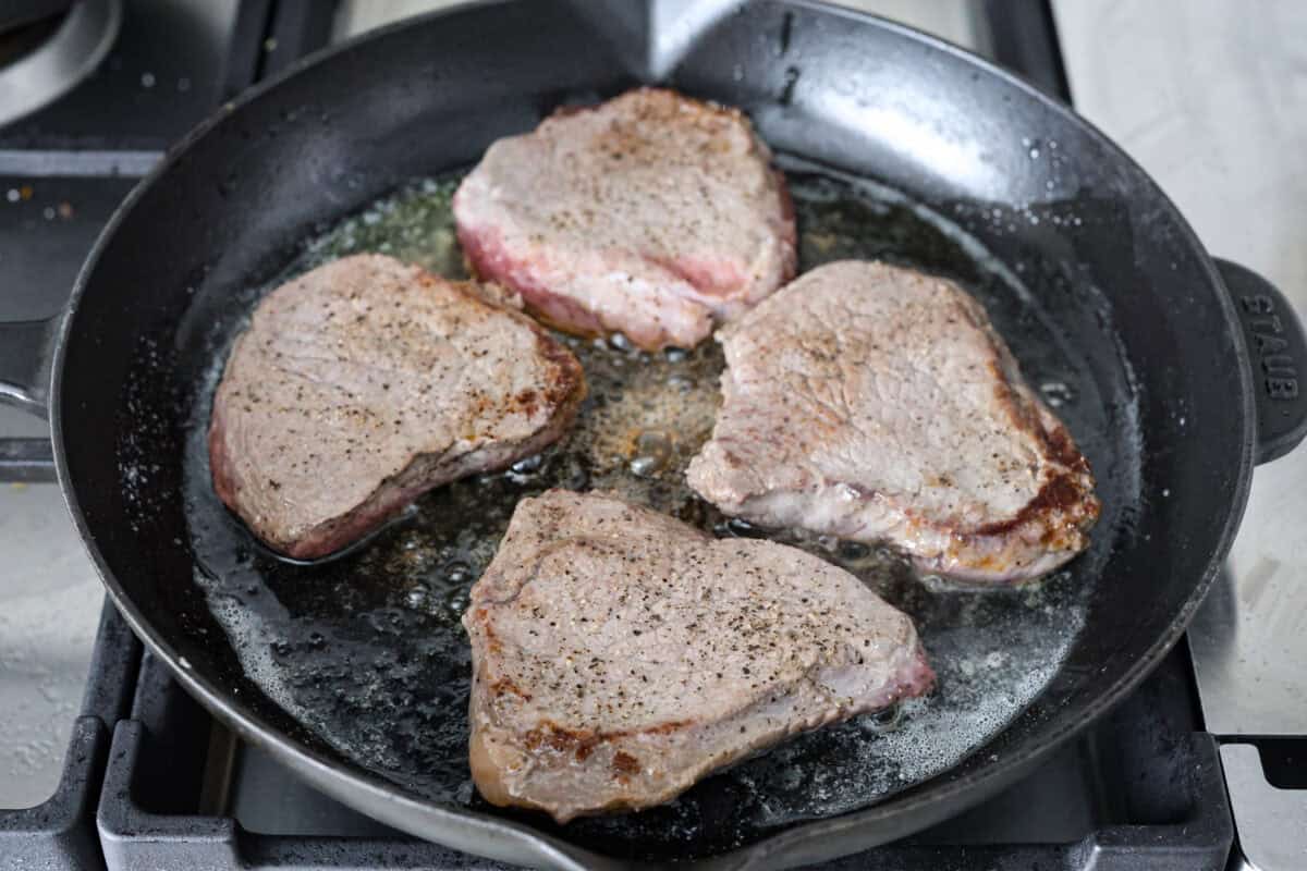 Angle shot of steaks cooking in a skillet. 