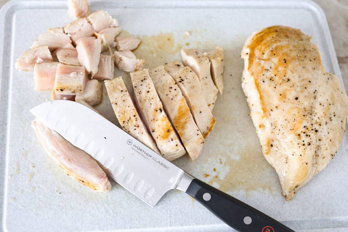 Overhead shot of partially cooked chicken being cut up on a cutting board. 