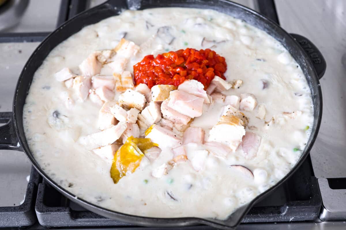 Angle shot of the pimentos, chicken, vinegar and bullion being added into the chicken a la kings sauce in the skillet. 