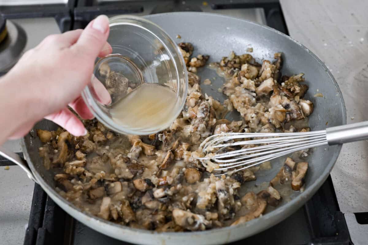 Angle shot of someone pouring chicken broth into the skillet with the flour and mushroom mixture. 