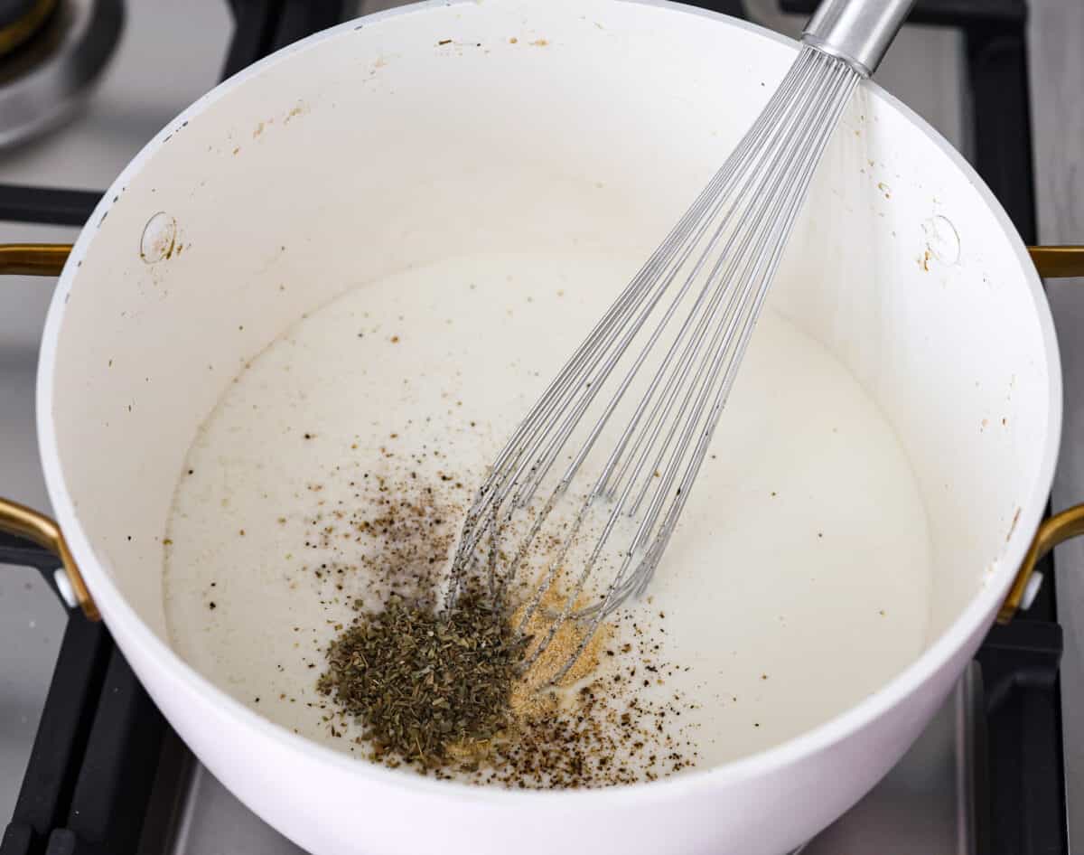 Overhead shot of seasonings being whisked into the white sauce. 