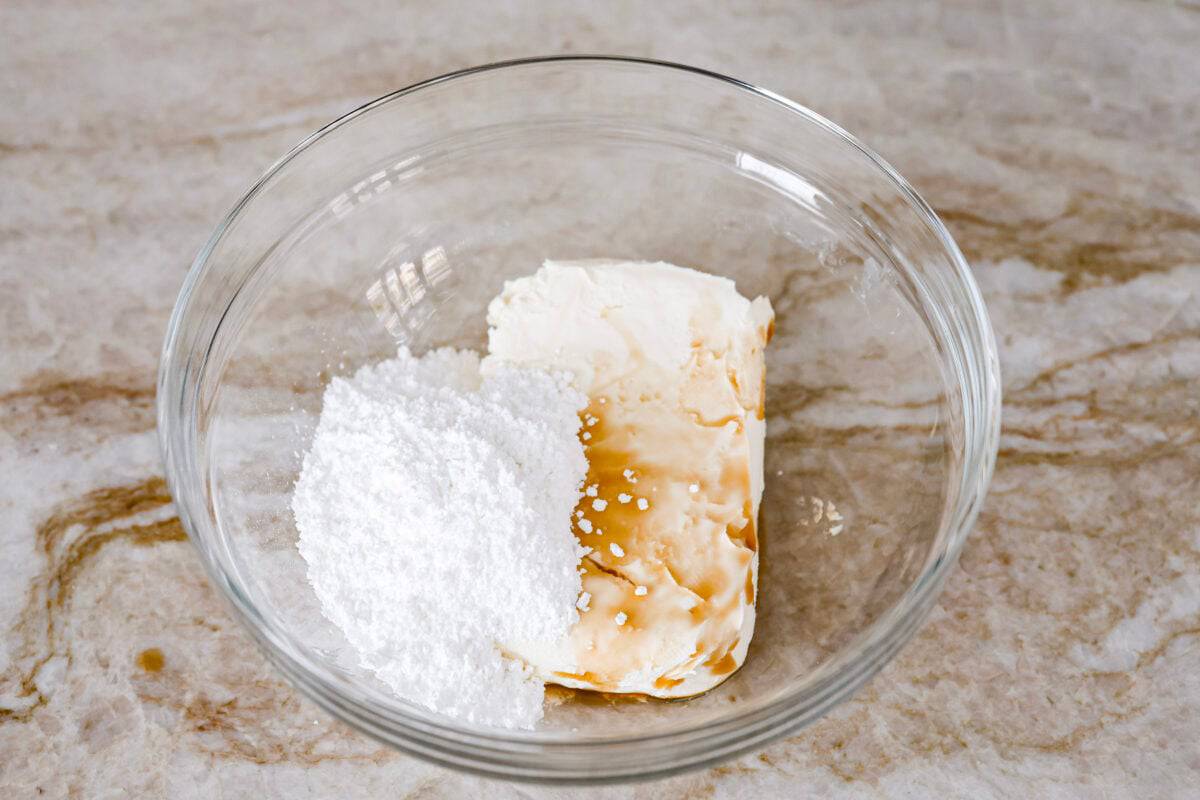 Overhead shot of cream cheese, powdered sugar and vanilla extract in a mixing bowl. 