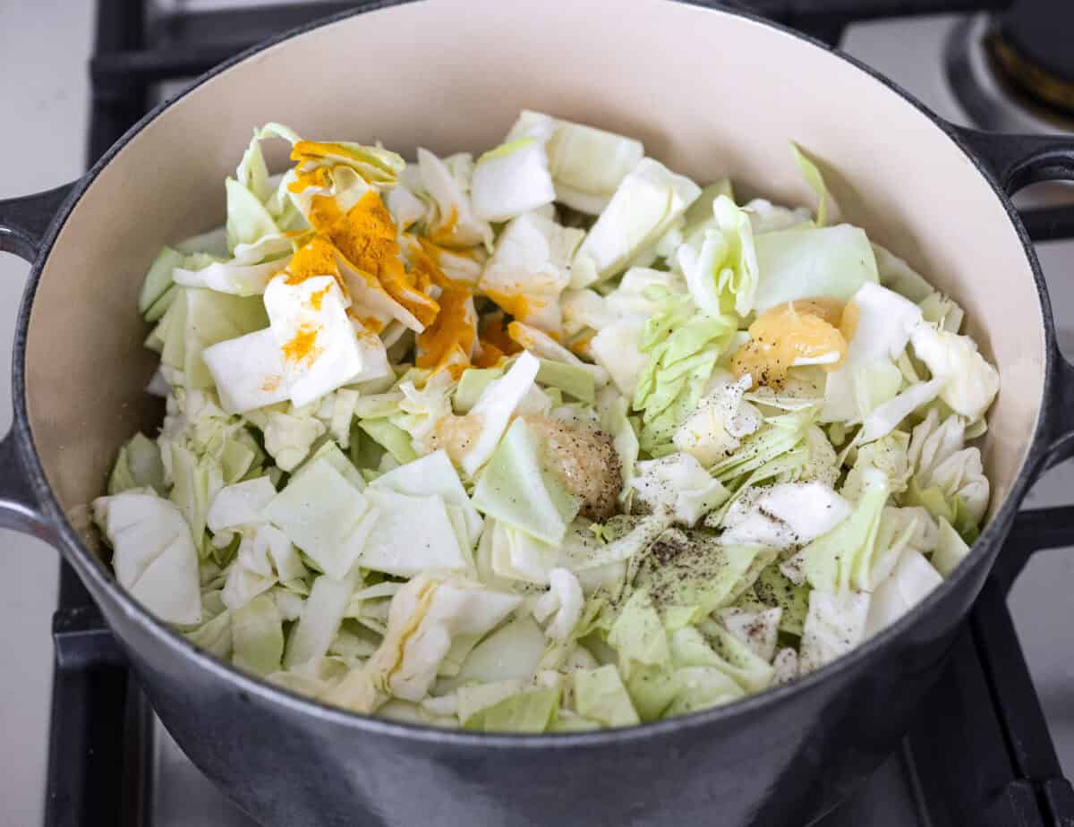 Overhead shot of the cabbage, turmeric, ginger, garlic, salt and pepper being added to the pot. 