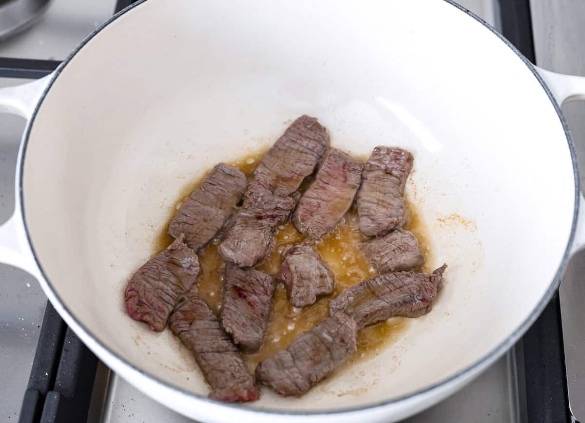 Overhead shot of beef searing in sesame oil in a pot. 