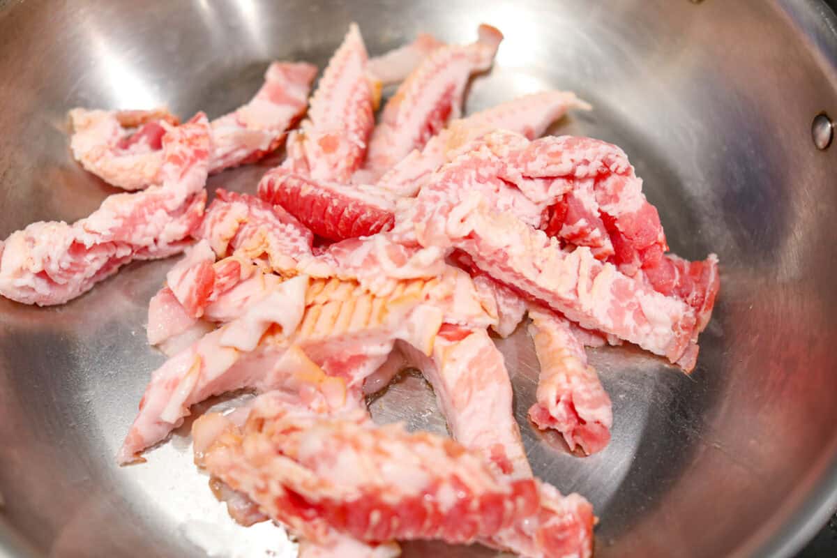 Overhead shot of diced bacon cooking in a skillet.