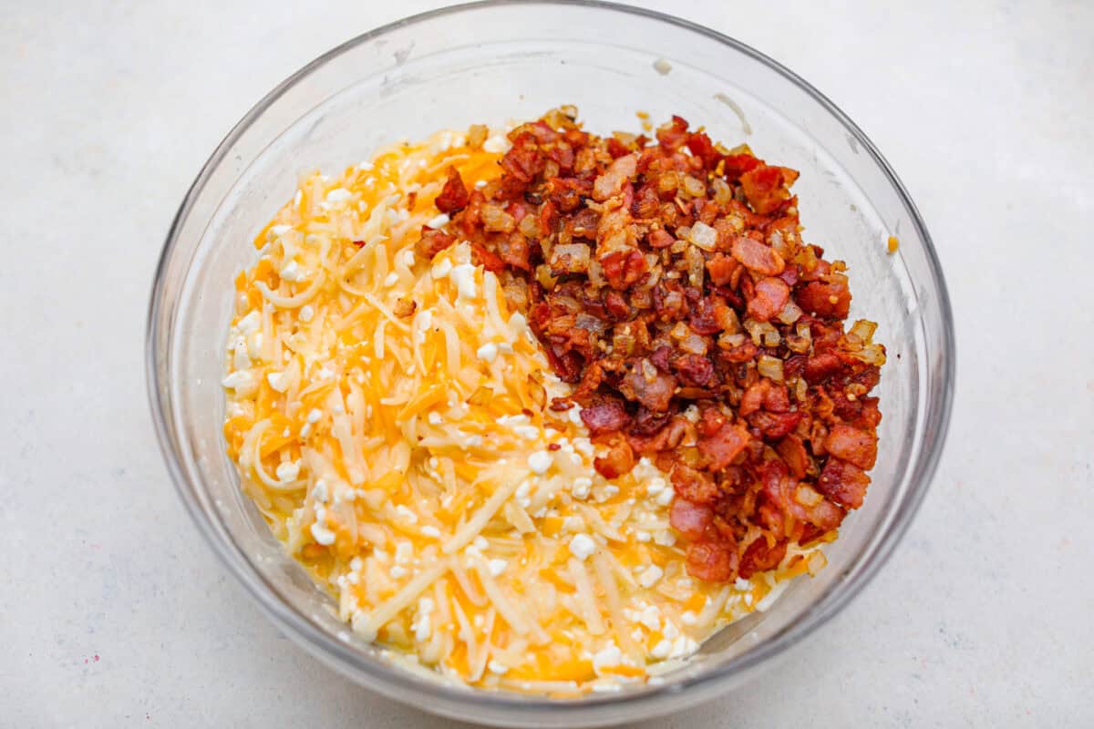 Overhead shot of the cheese and potato mixture with bacon and onion mixture in a bowl. 