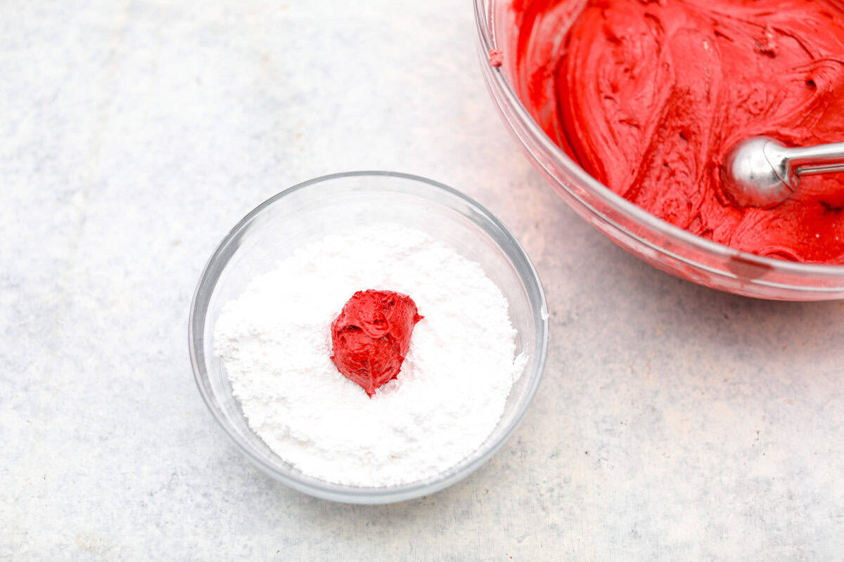 Overhead shot of a scoop of dough in a bowl of powdered sugar. 