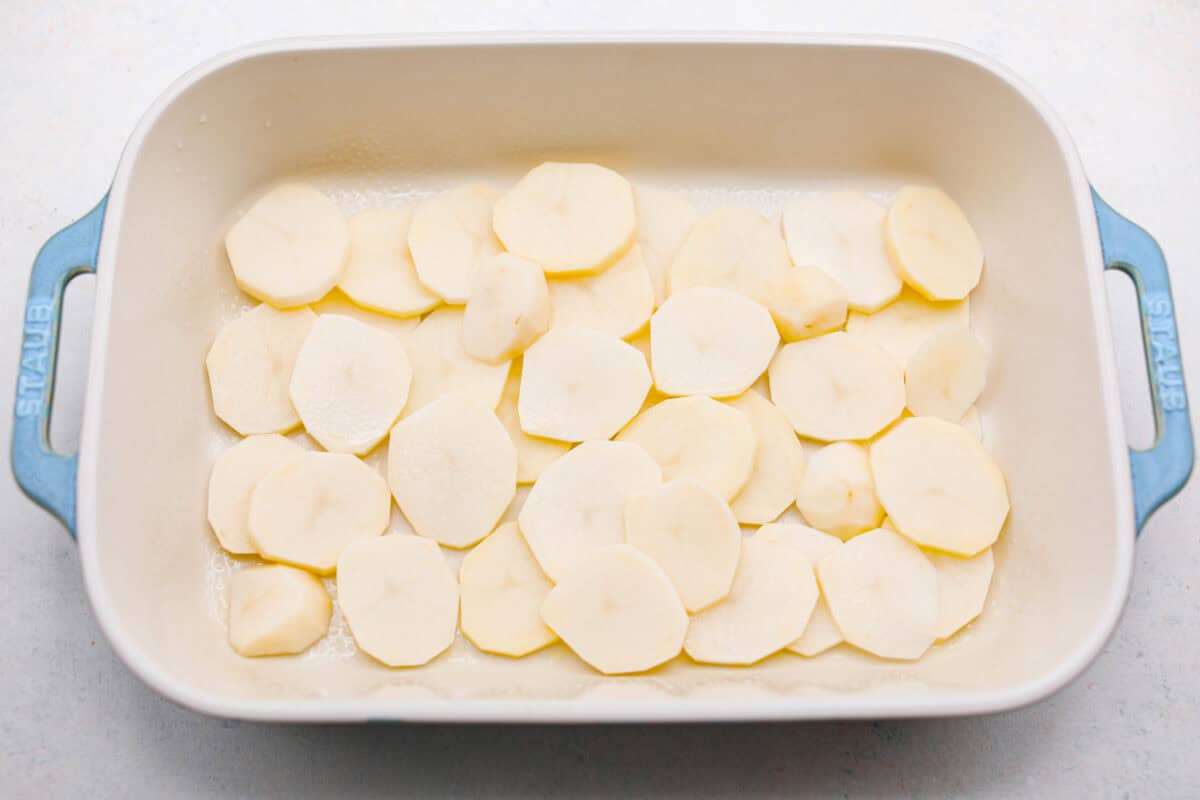 Overhead shot of potato slices in the bottom of a baking dish. 