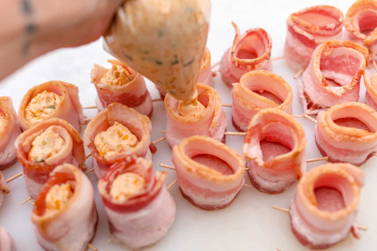 Overhead shot of someone adding filling to the top of the bacon wrapped pork slices.