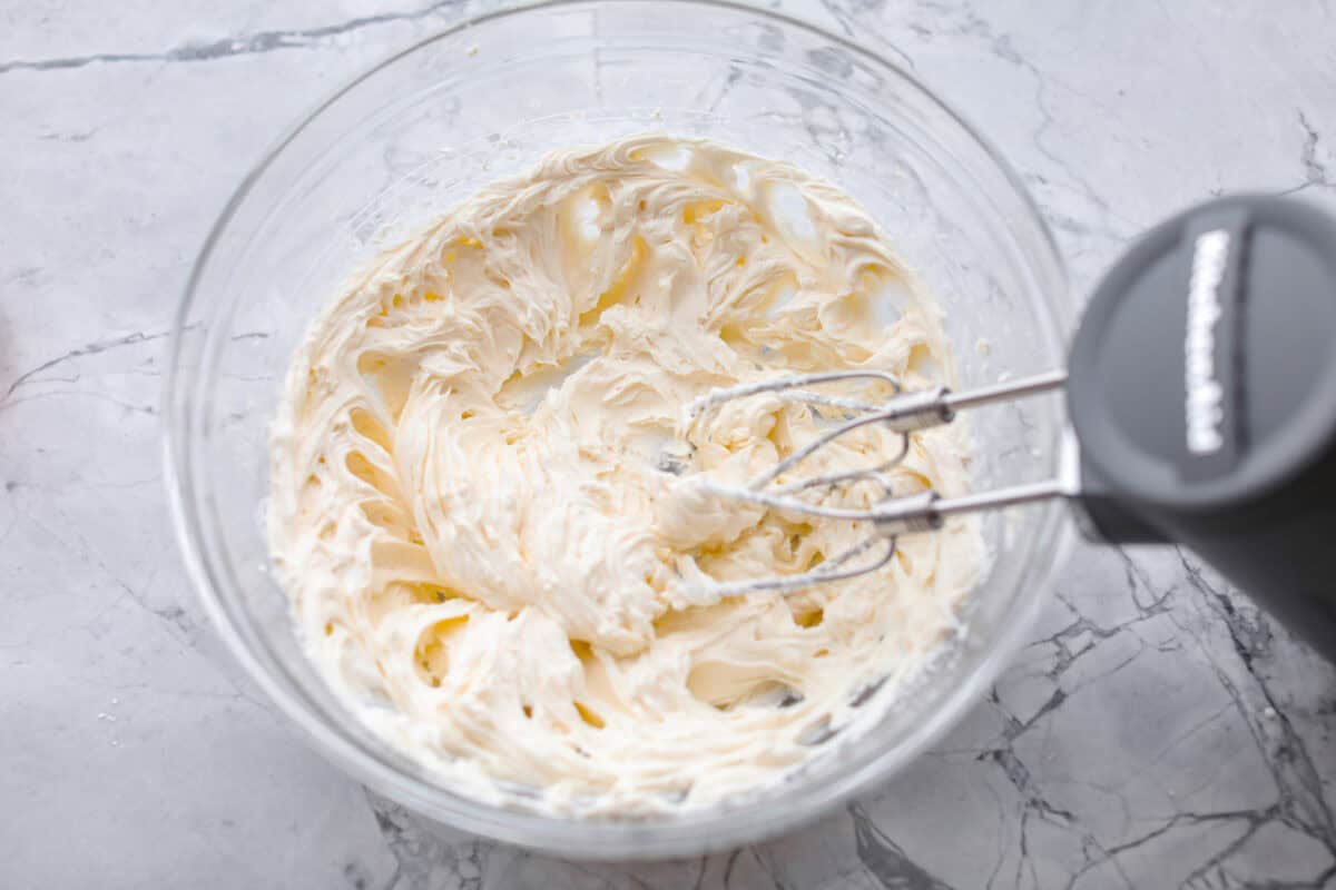 Overhead shot of the powdered sugar, vanilla and heavy cream being mixed in with the cream cheese. 