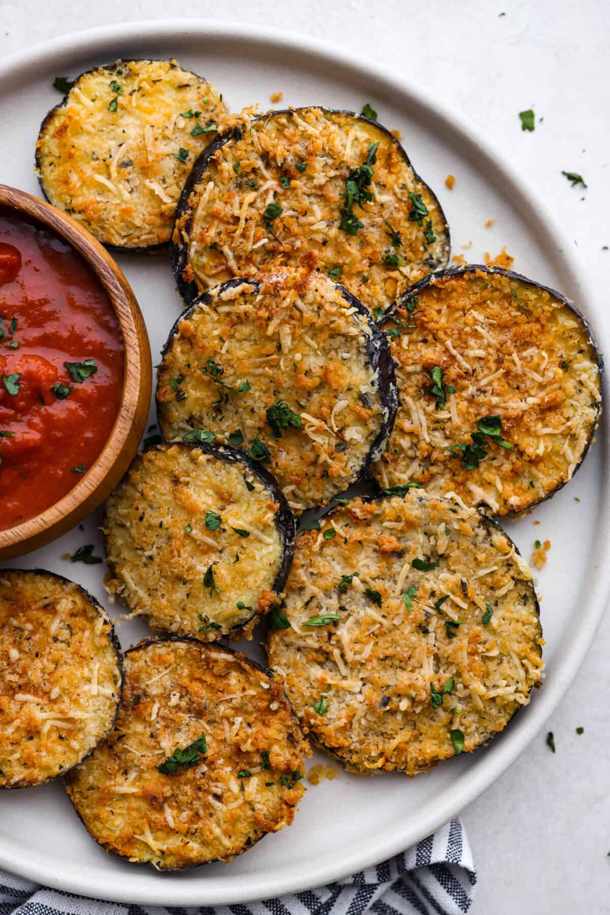 Overhead shot of plated air fryer eggplant with a bowl of marinara sauce next to the slices. 