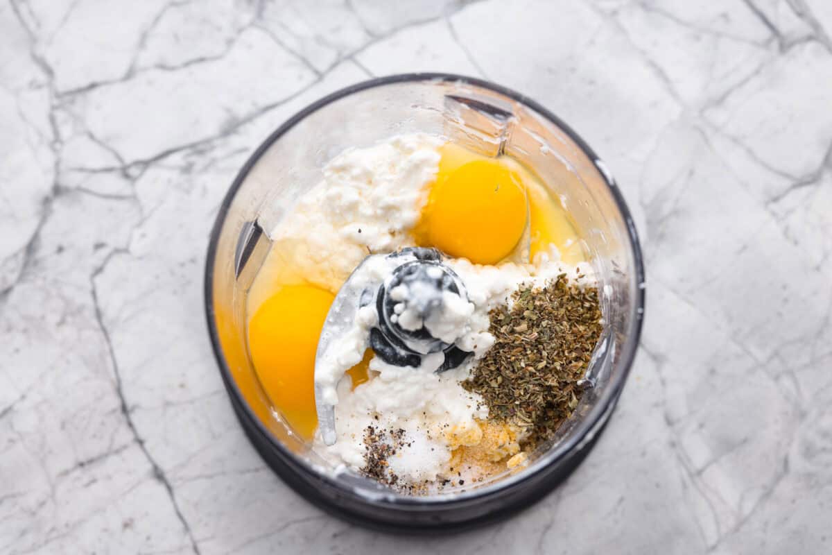 Overhead shot of cottage cheese, eggs and seasonings in a food processor. 