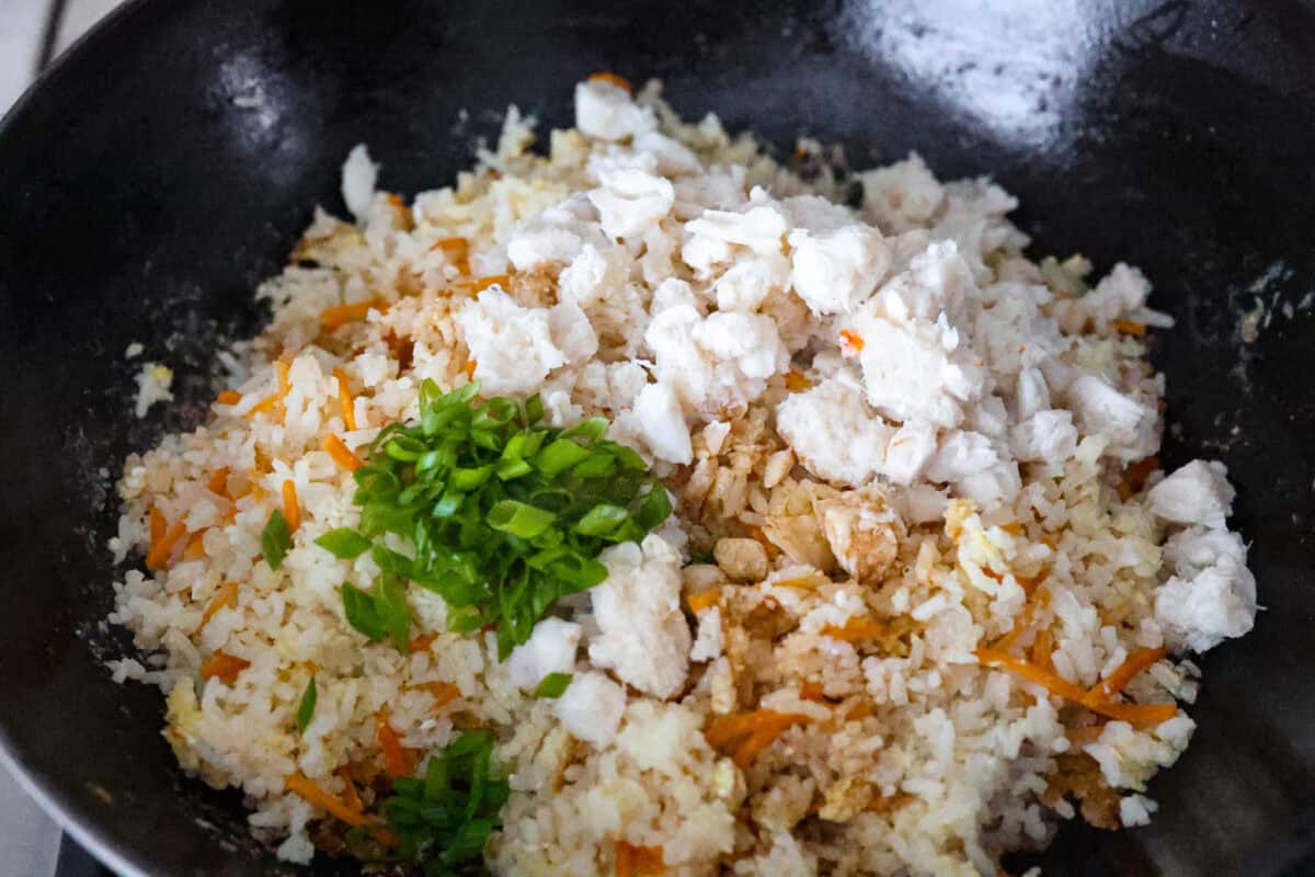 Angle shot of the crab, green onions, soy sauce and lime juice on top of the rice, veggie and egg mixture. 