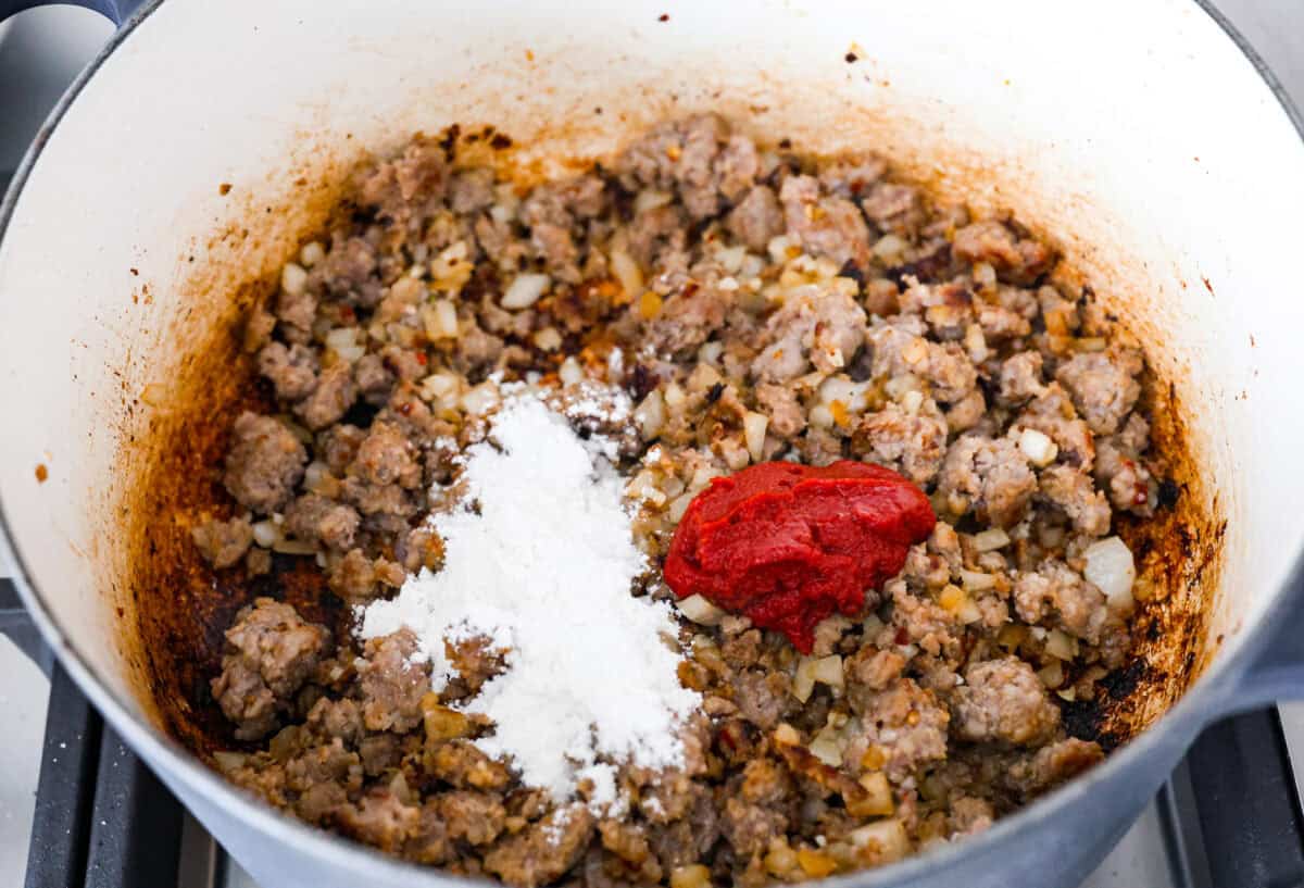 Overhead shot of sausage and onions with flour and tomato paste added to it. 