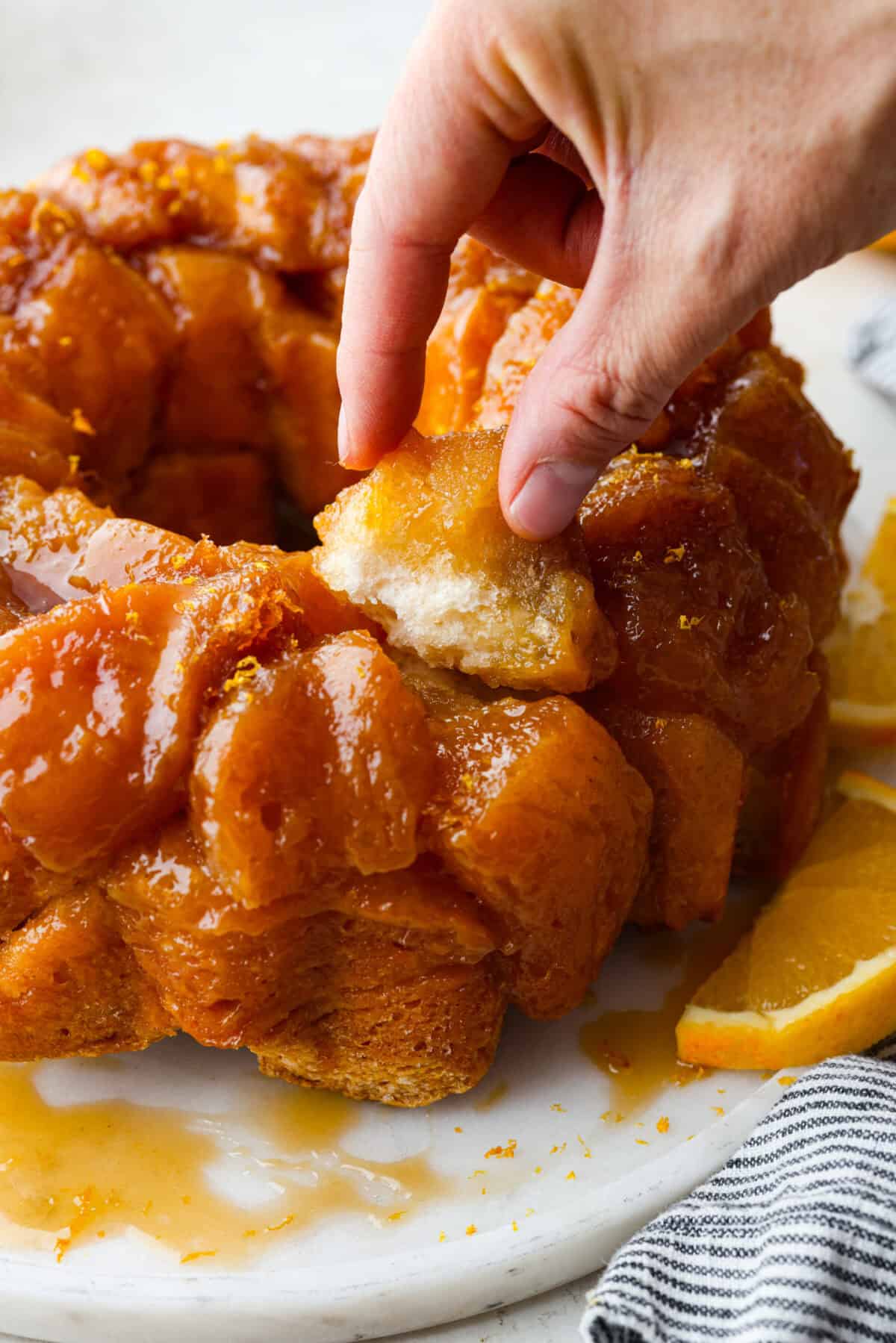 Close up shot of someone pulling a piece of orange monkey bread off the whole bundt. 