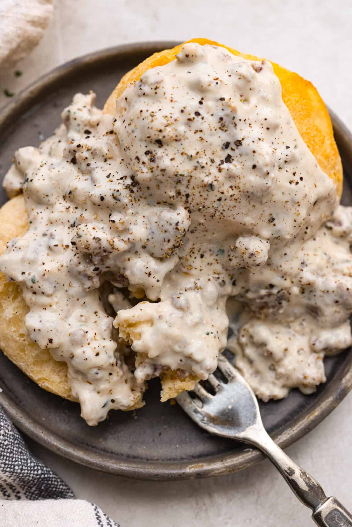 Overhead shot of sausage gravy over a fluffy biscuit on a plate. 