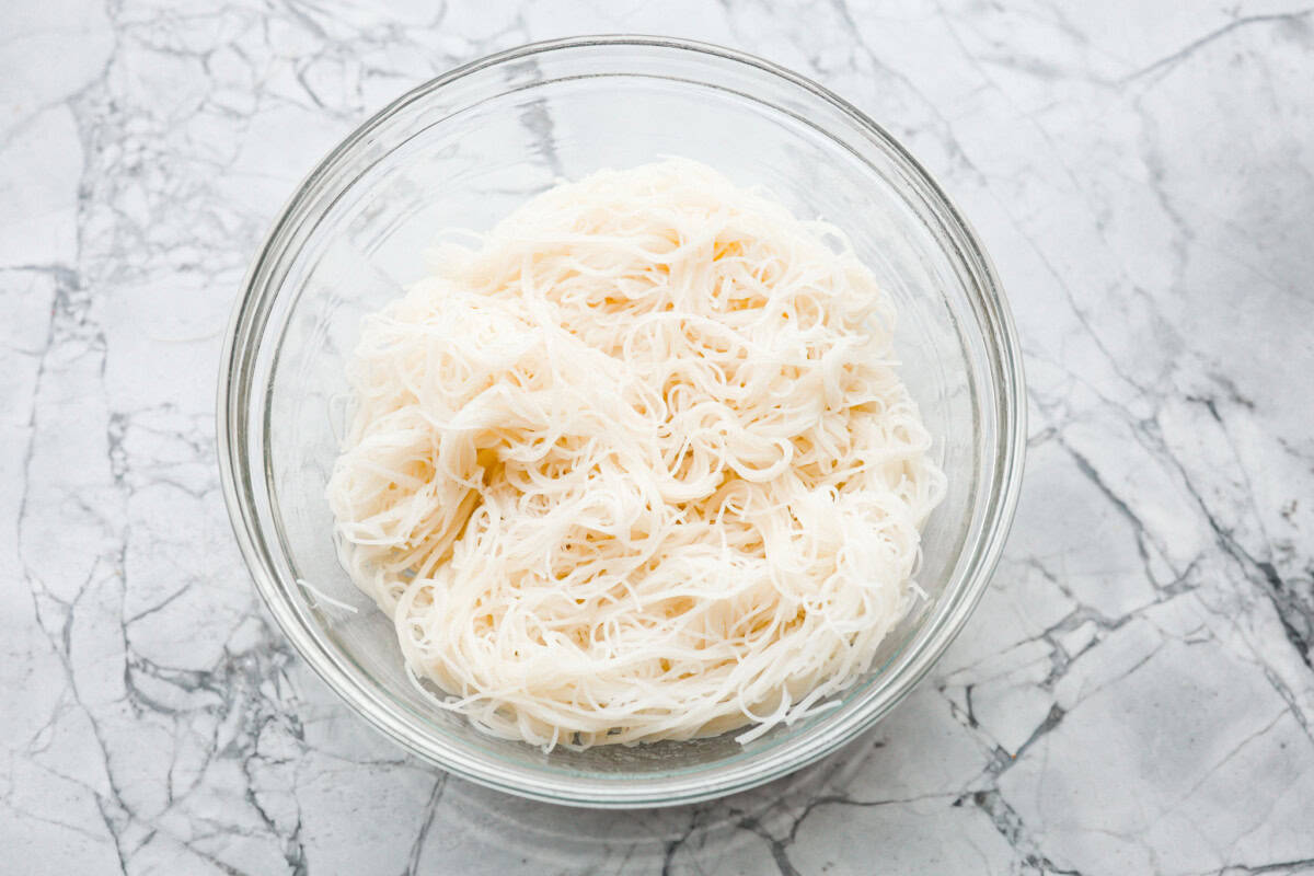 Overhead shot of cooked vermicelli noodles in a bowl with sesame oil. 