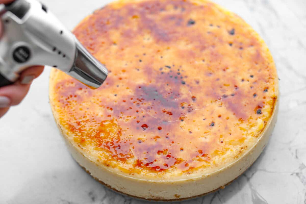 Overhead shot of someone torching the sugar on top of the creme brûlée cheesecake. 