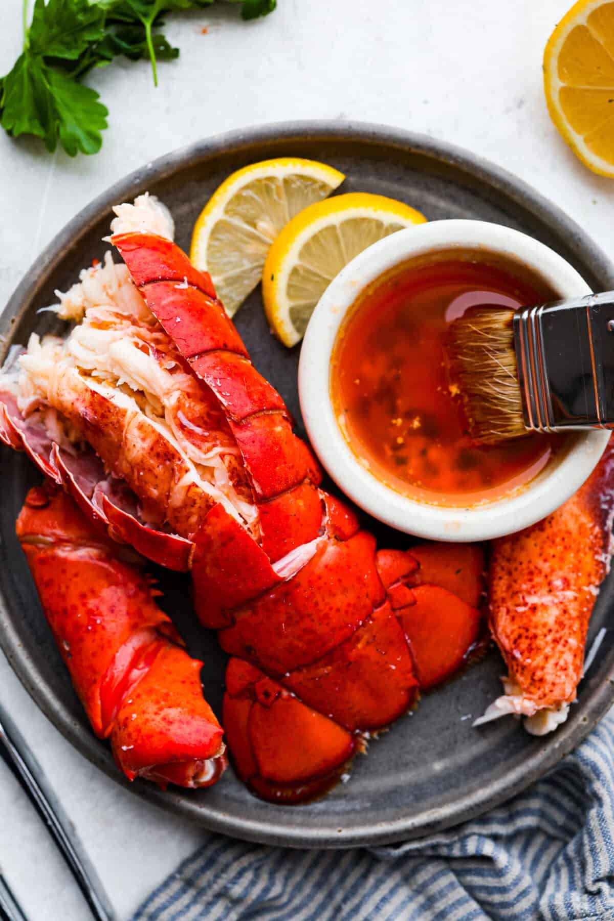 Overhead shot of a lobster tail, meat from the claw and leg on a plate with a small bowl of melted butter. 