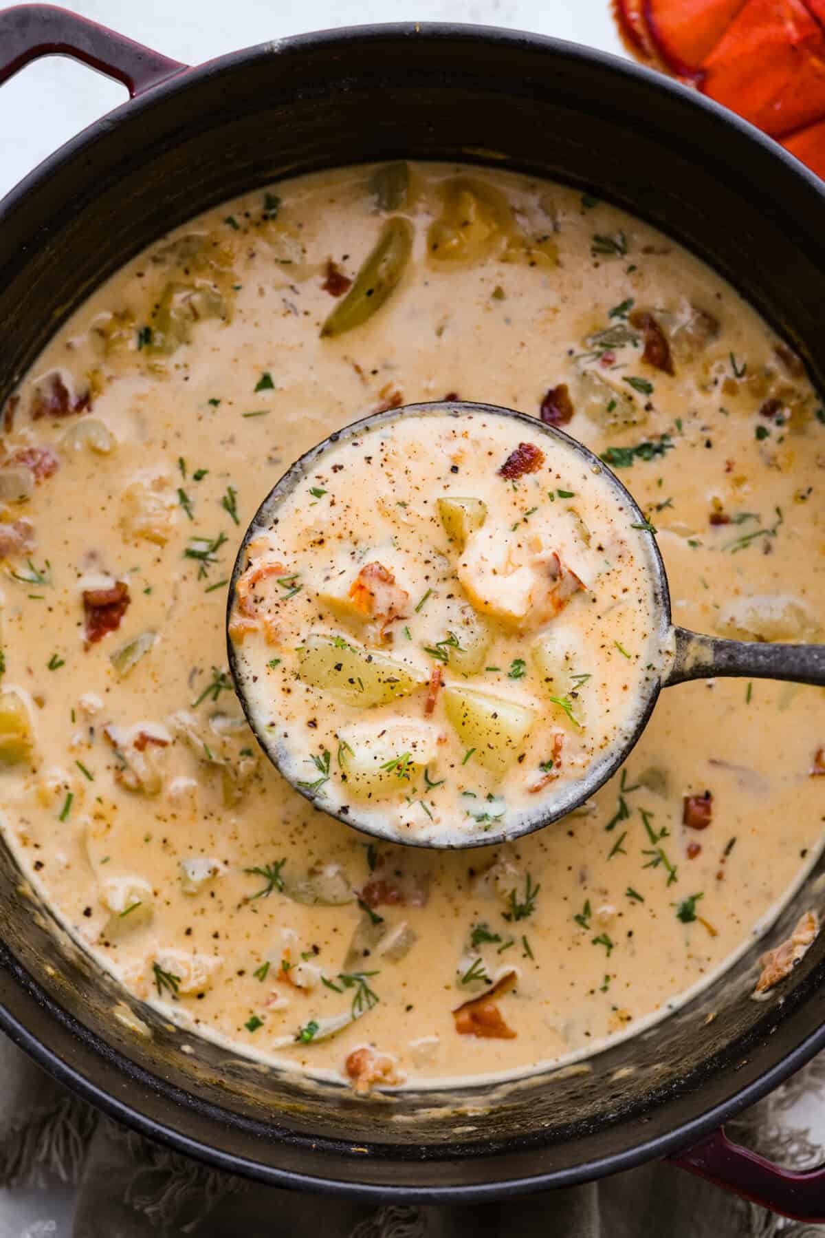 Overhead shot of lobster chowder in a pot with a ladle.