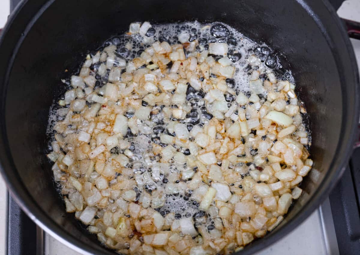 Overhead shot of onions and garlic cooking in bacon grease. 